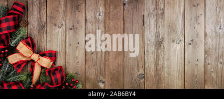 Christmas corner border banner with red and black checked buffalo plaid ribbon, burlap and tree branches. Top view on a rustic wood background. Stock Photo