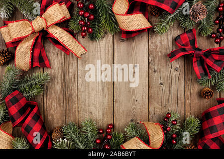 Christmas frame with red and black checked buffalo plaid ribbon, burlap and tree branches. Top view on a rustic wood background. Stock Photo