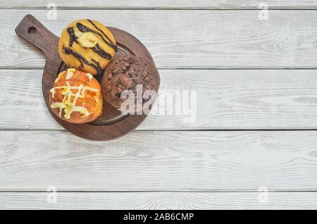 Sweet and tasty snack. Three different colorful cupcakes on a wooden background. Stock Photo
