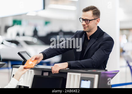 Side view of handsome man wearing glasses giving passport to staff at check in desk at airport Stock Photo