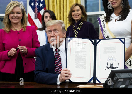 Washington, District of Columbia, USA. 25th Nov, 2019. US President Donald J. Trump (C) holds up 'the Women's Suffrage Centennial Commemorative Coin Act', after signing it during a ceremony, beside United States Senator Marsha Blackburn (Republican of Tennessee) (L), in the Oval Office of the White House in Washington, DC, USA, 25 November 2019. Trump signed 'H.R. 2423, the Women's Suffrage Centennial Commemorative Coin Act'  Stock Photo