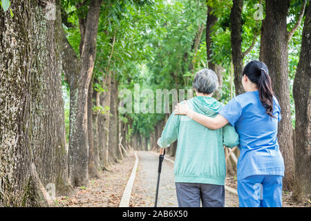 Smiling nurse helping senior woman to walk around the park Stock Photo