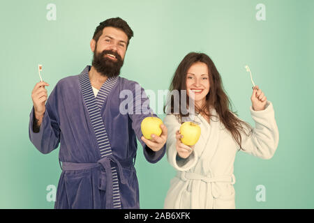 Couple in love cleaning teeth. Freshness and cleanliness. Keep teeth healthy. Healthy habits. Brush teeth every morning. Oral hygiene. Couple bathrobes hold toothbrushes and apples. Personal hygiene. Stock Photo