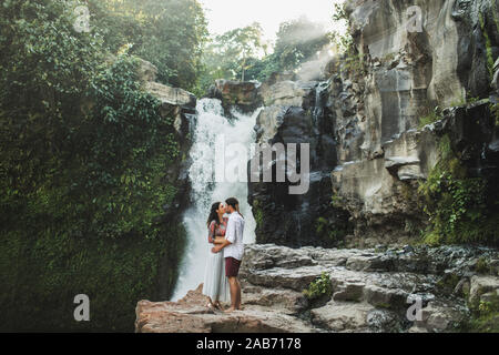 Young couple in love kissing with amazing view of Tegenungan cascade waterfall. Happy together, honeymoon in Bali. Travel lifestyle. Stock Photo