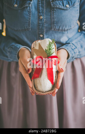 Close up of woman's hands holding homemade stollen christmas cake wrapped as a gift. Selective focus. Stock Photo