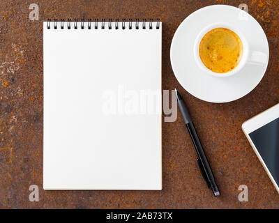 clean white sheet in an open spiral-bound pad, pen, mobile phone and Cup of coffee on the iron of the rusty metal table, top view Stock Photo