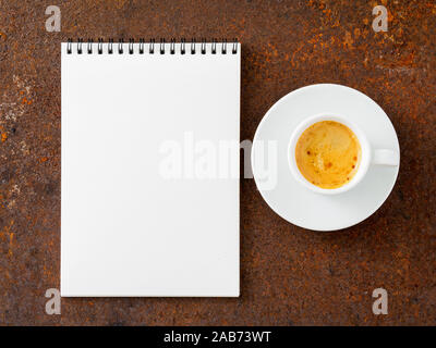 blank sheet of notebook with a spiral and cup of coffee on rusted old iron table, top view. Stock Photo
