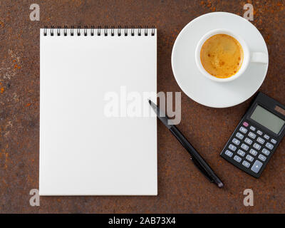 clean white sheet in an open spiral-bound pad, pen, calculator and Cup of coffee on the iron of the rusty metal table, top view Stock Photo