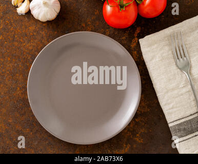clean empty gray plate and fork on linen napkin on rusted old iron table Stock Photo