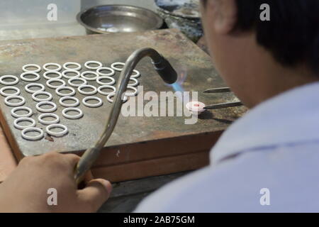 Close up of a men goldsmith working and shaping an unfinished ring with a tool at workbench in workshop. Stock Photo