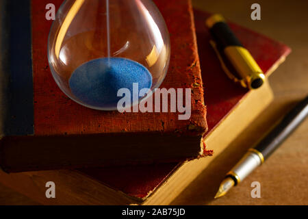 Hourglass on old book in morning light. Time of reading a book. Stock Photo