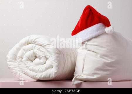 Close-up of a rolled duvet and a pillow with a cap of Santa Claus lying on the chest, on the background light walls. Stock Photo