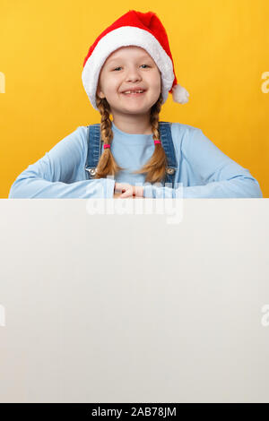 Happy child in santa hat is holding a blank space banner on a yellow background. Christmas card. Stock Photo