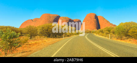 Panorama of road leading to domed rock formations in Uluru-Kata Tjuta National park at vibrant color of sunset. Northern Territory, Australia Stock Photo