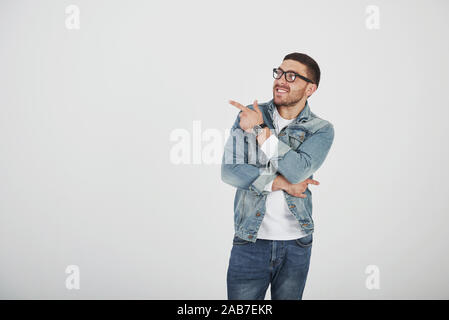Happy excited bearded man in eyeglasses looking at camera with smile and pointing away at copy space with two fingers isolated over white background Stock Photo