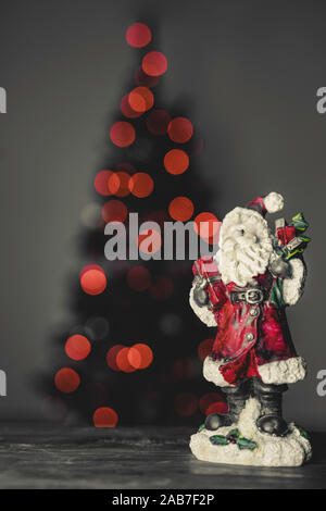 Close up image of a ceramic Santa Claus figure. Out of focus christmas three in the background. Bokeh of christmas lights. Stock Photo
