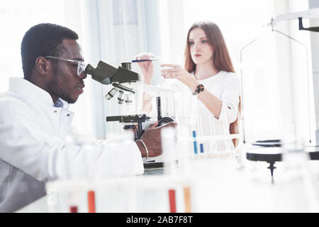 The scientist works with a microscope in a laboratory conducting experiments and formulas. Stock Photo