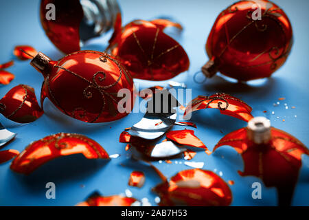 Bright orange, glass Christmas baubles broken, scattered fragments on a blue background Stock Photo