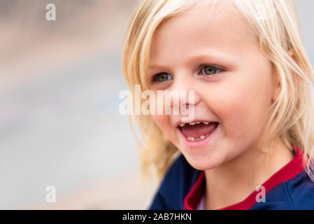 A cute, pretty little blonde haired girl wearing a football shirt being cheeky, smiling and having lot's of fun outdoors in the UK countryside Stock Photo