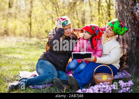A younger woman is with her elderly mother in a garden. She is smiling at the woman who is holding tablet and a pen, and looking back at her. Horizont Stock Photo