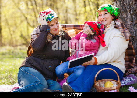 A younger woman is with her elderly mother in a garden. She is smiling at the woman who is holding tablet and a pen, and looking back at her. Horizont Stock Photo