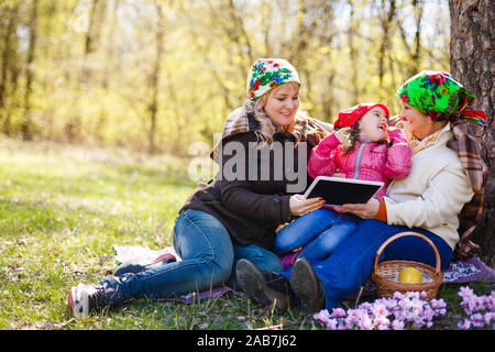 A younger woman is with her elderly mother in a garden. She is smiling at the woman who is holding tablet and a pen, and looking back at her. Horizont Stock Photo