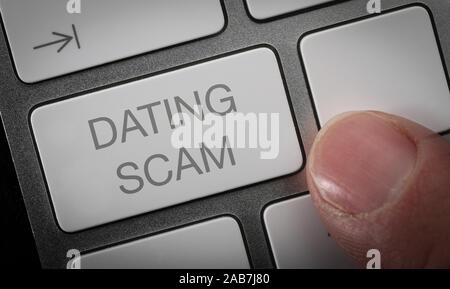 A man pressing a key on a computer keyboard with the words dating scam. Online dating scam concept image. Stock Photo
