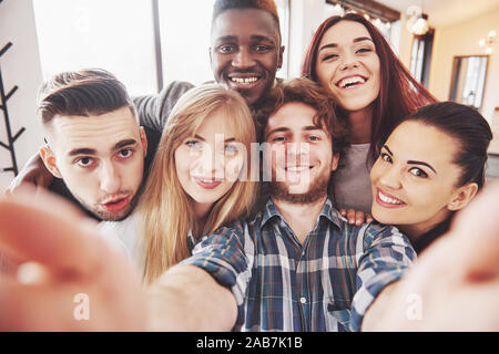 Friends having fun at restaurant. Three boys and three girls making selfie and laughing. On foreground boy holding smart phone. All wear casual Stock Photo