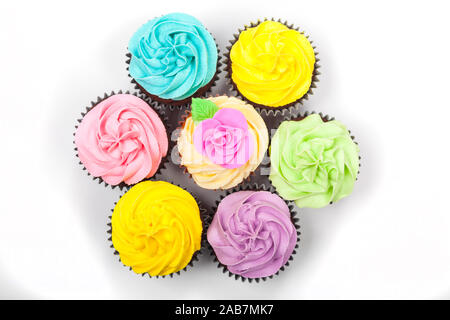 Overhead flat lay cupcakes or cup cakes with icing or frosting, pink, yellow, purple, blue and cream with green leaves, rose and floral decorations ph Stock Photo