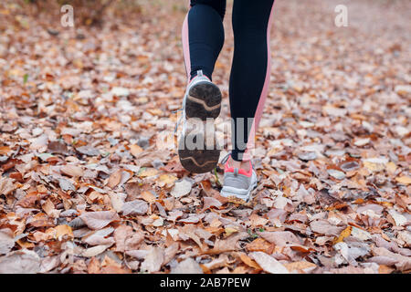 Close-up of feet of a runner running in autumn leaves in park