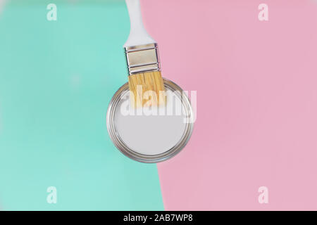 Open can with white paint and brush on mint and pink pastel background. Stock Photo