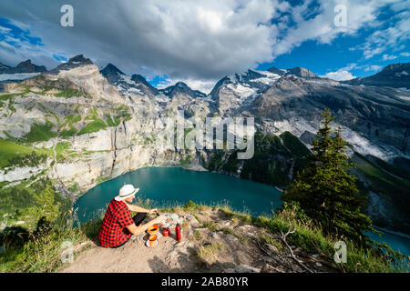 Hiker cooking food on camping stove high up above Oeschinensee lake, Bernese Oberland, Kandersteg, Canton of Bern, Switzerland, Europe Stock Photo