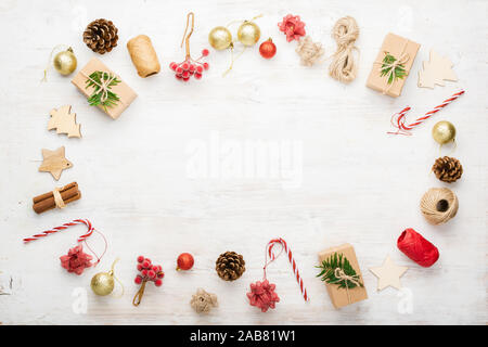 Creative Christmas background of various objects including gift boxes, cinnamon sticks, decorative berries on white wooden table, copy space in the middle, on white table, selective focus Stock Photo
