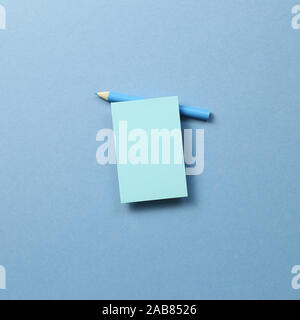 Blue memo note pad and blue colored pencil on blue background Stock Photo