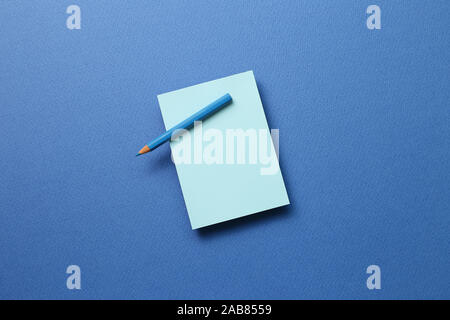 Blue memo note pad and blue colored pencil on blue background Stock Photo