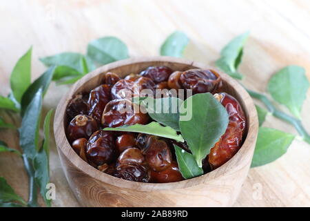 Wooden bowl full of dried dates with herb leaves. Sweet fruit - fruits of the date palm (Phoenix dactylifera). Brown bowl on teak table. Stock Photo