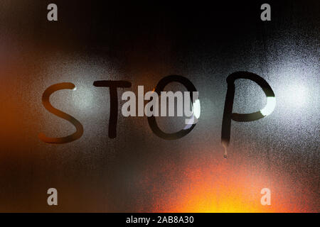 the word stop written on night wet window glass close-up with blurred background. Stock Photo