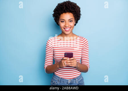 Photo of pretty dark skin lady holding telephone hands reading new post comments likes reposts wear casual striped sweater jeans isolated blue color Stock Photo