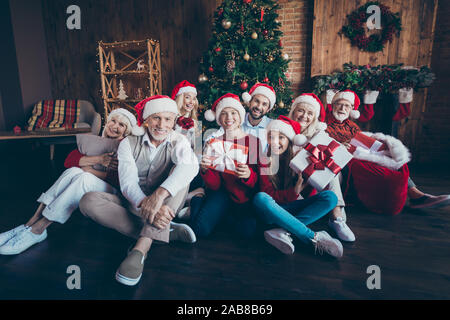 Photo of friendly big large family smiling toothily having new year party together sitting on floor in santa cap headwear children in childhood in