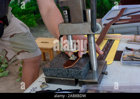 A man using a leather punch while working with a belt on the street, closeup Stock Photo