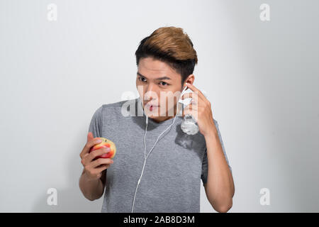Portrait of handsome Asian sportsman in gray shirt holds water and apple over white background.