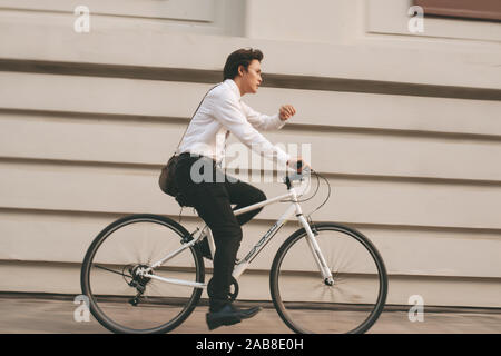 Hurry Asian businessman riding bike in rush hour.  Young man late for train work, meeting. Office life and business competition. Stock Photo