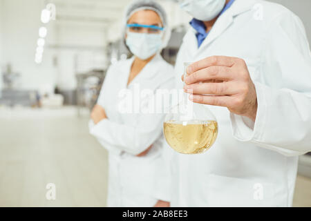 Technologist worker in masks and coats look at the liquid in the flask at work. Stock Photo