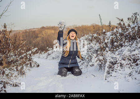 winter girl throwing snowball at camera smiling happy having fun outdoors on snowing winter day playing in snow. Cute playful young woman outdoor Stock Photo