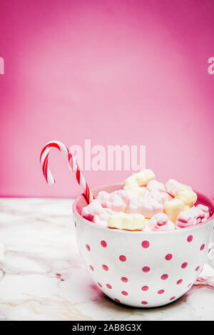 Pink white mug with marshmallows, sugar cane on a marble surface with pink background Stock Photo