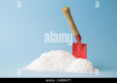 Red shovel standing upright in small pile of snow on pastel blue background minimal creative winter concept. Space for copy. Stock Photo