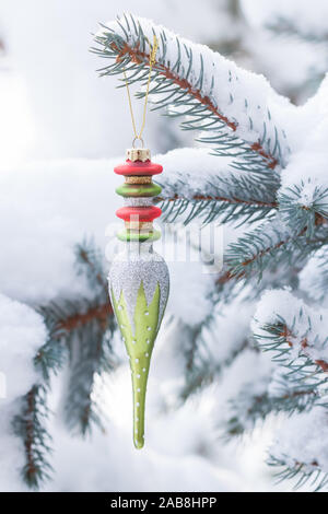 A close up view of a beautiful Christmas ornament hanging on a snowy pine tree branch outside on a sunny day. Stock Photo