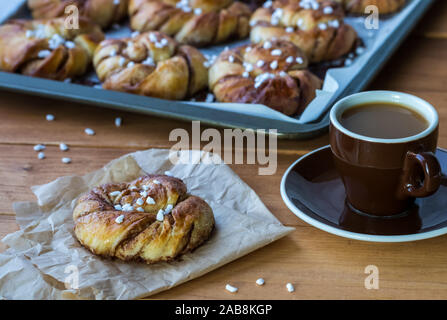A fresh batch of Swedish cinnamon buns with one roll on parchment paper beside a cup of coffee. Stock Photo