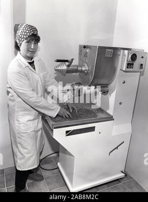 1980s, historical, a female worker in overalls and headscarf, using an Italian made machine at a food factory, to make pasta, fusilli, Yorkshire, England, UK. Stock Photo