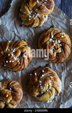 Top down view of homemade Swedish Kanelbullar cinnamon buns with pearl sugar on parchment paper. Stock Photo